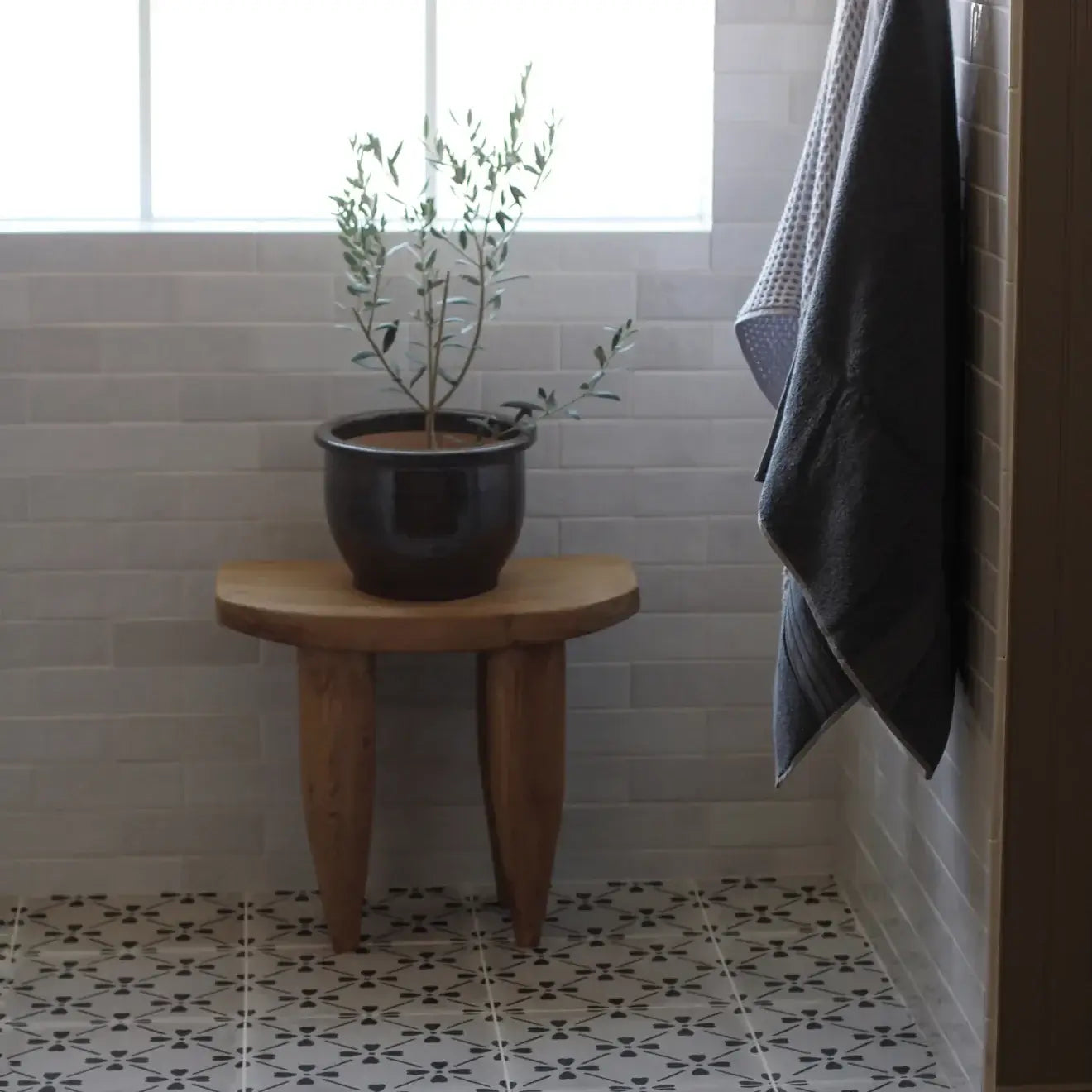 Stylish bathroom corner featuring a wooden stool, potted plant, and gray towels against a bright tiled wall.