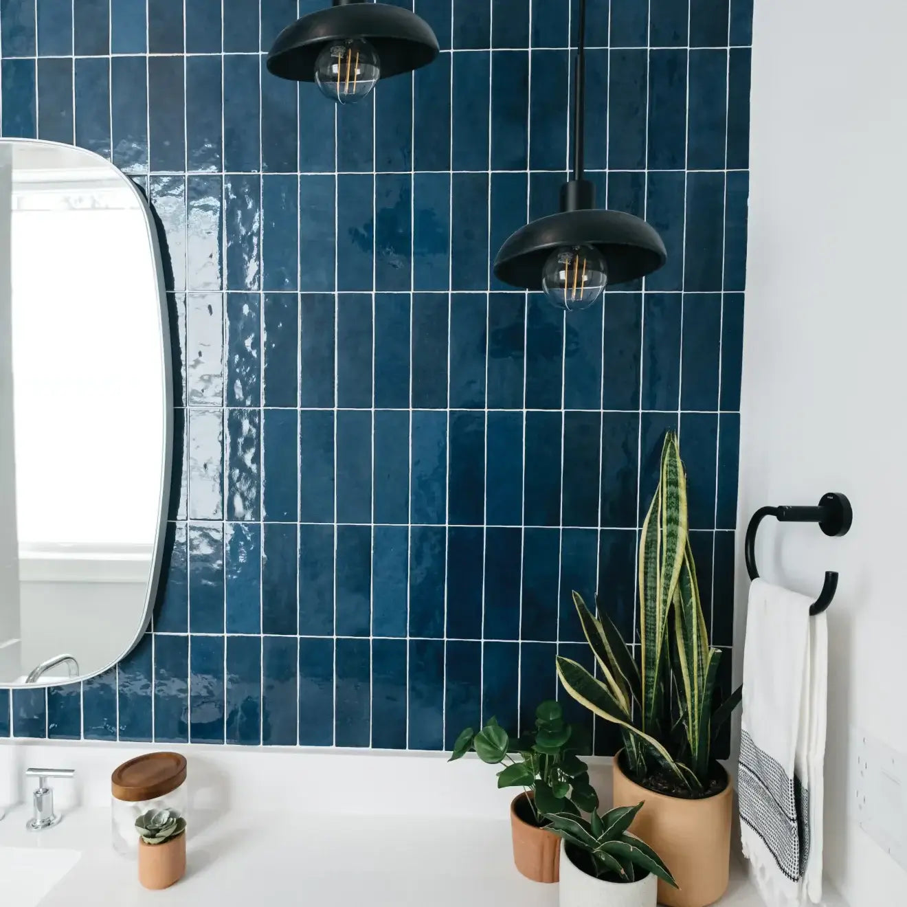 Modern bathroom with Cloé 2.5" x 8" glossy blue ceramic tile, plants, mirror, and black pendant lights.