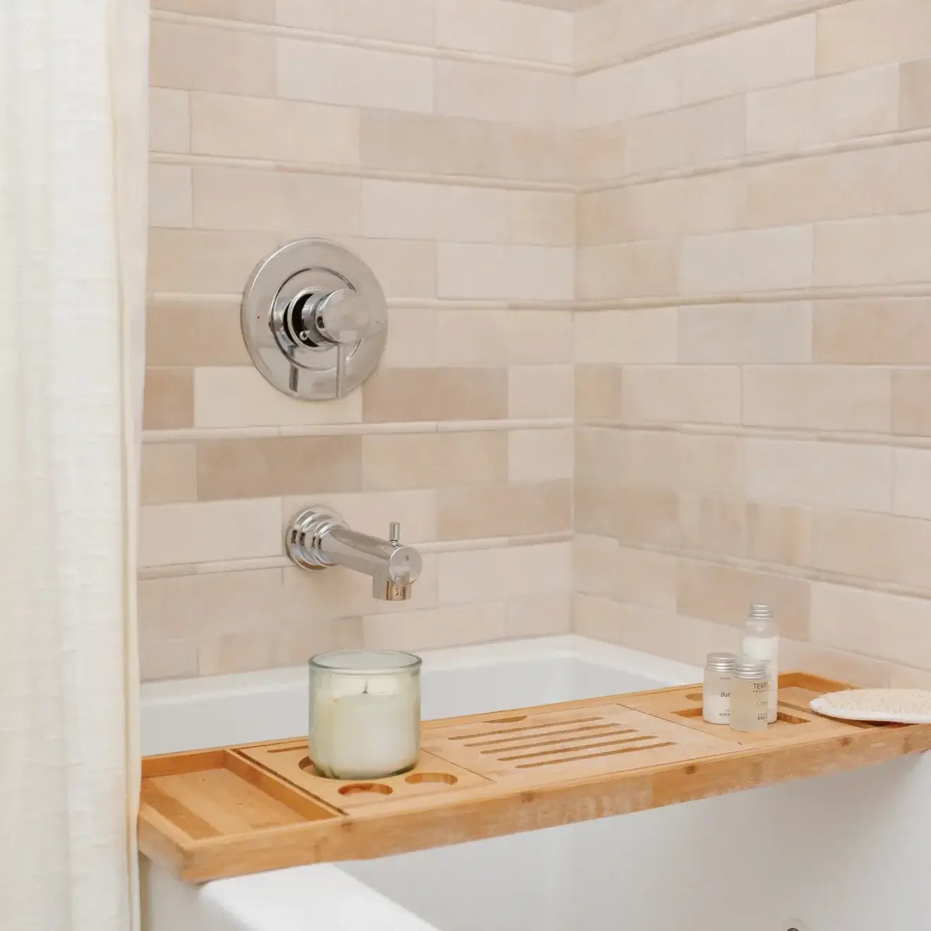 Luxurious bathroom featuring Cloé glossy creme ceramic tile, chrome fixtures, and a bamboo bath tray with candles.