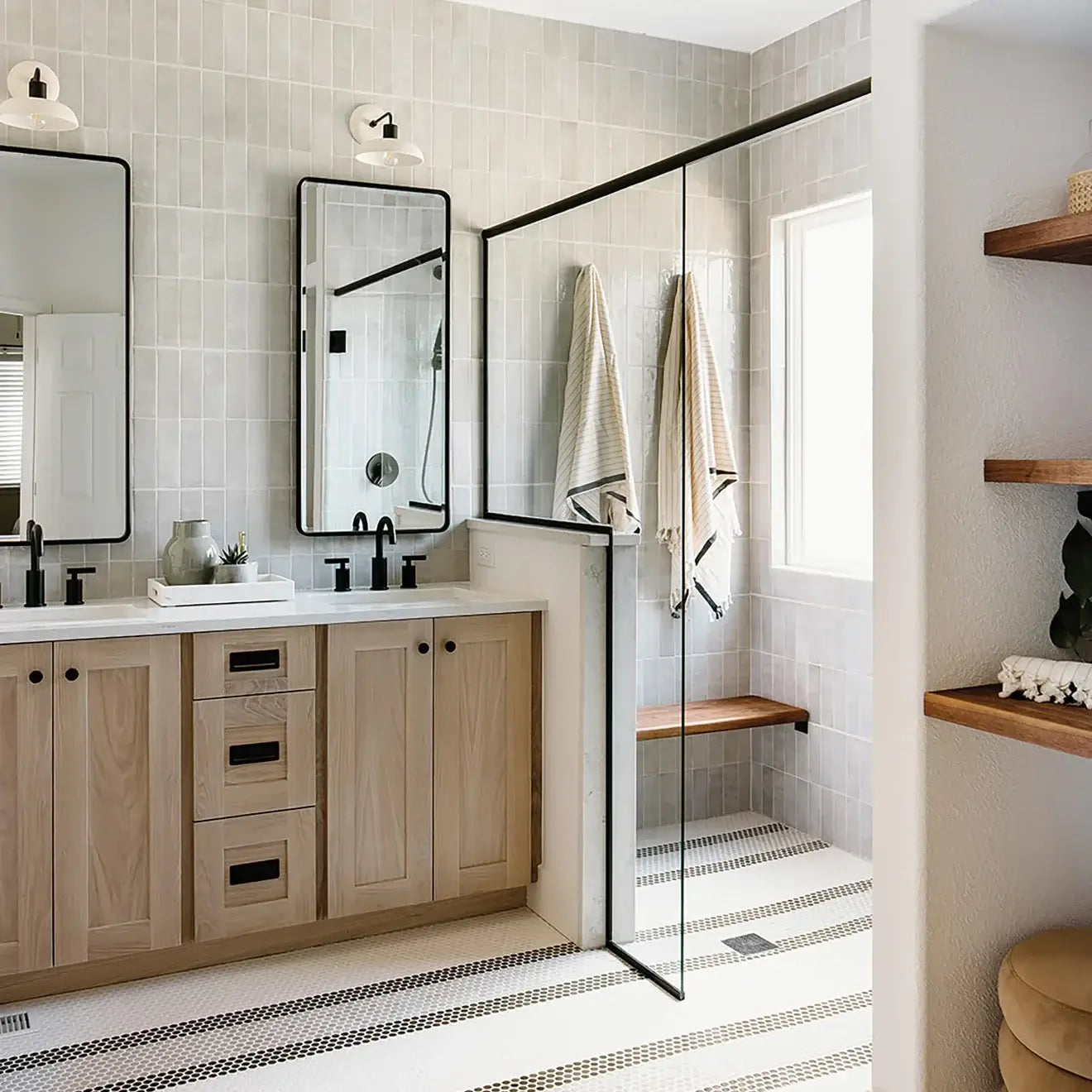 Modern bathroom with large mirrors, wooden vanity, and a glass shower, featuring light grey tiles and stylish decor.