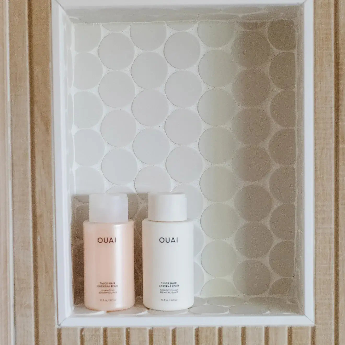 OUAI hair products in a niche with round white mosaic tile background, showcasing a chic bathroom design.
