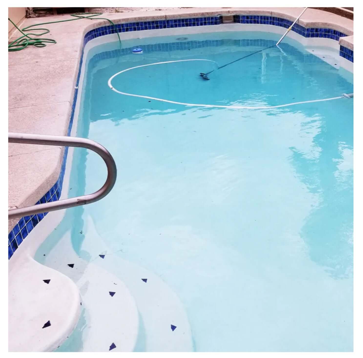 Clear swimming pool with blue tiled edges and cleaning equipment, showcasing a clean and inviting aquatic space.