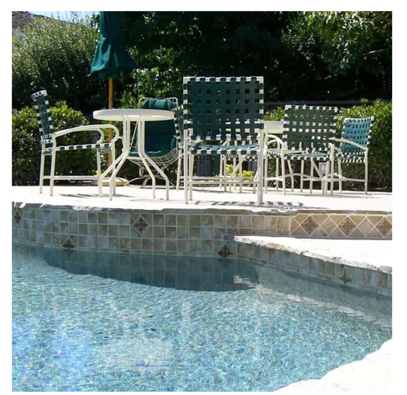 Relaxing poolside area featuring turquoise chairs and table near clear water with lush greenery in the background.