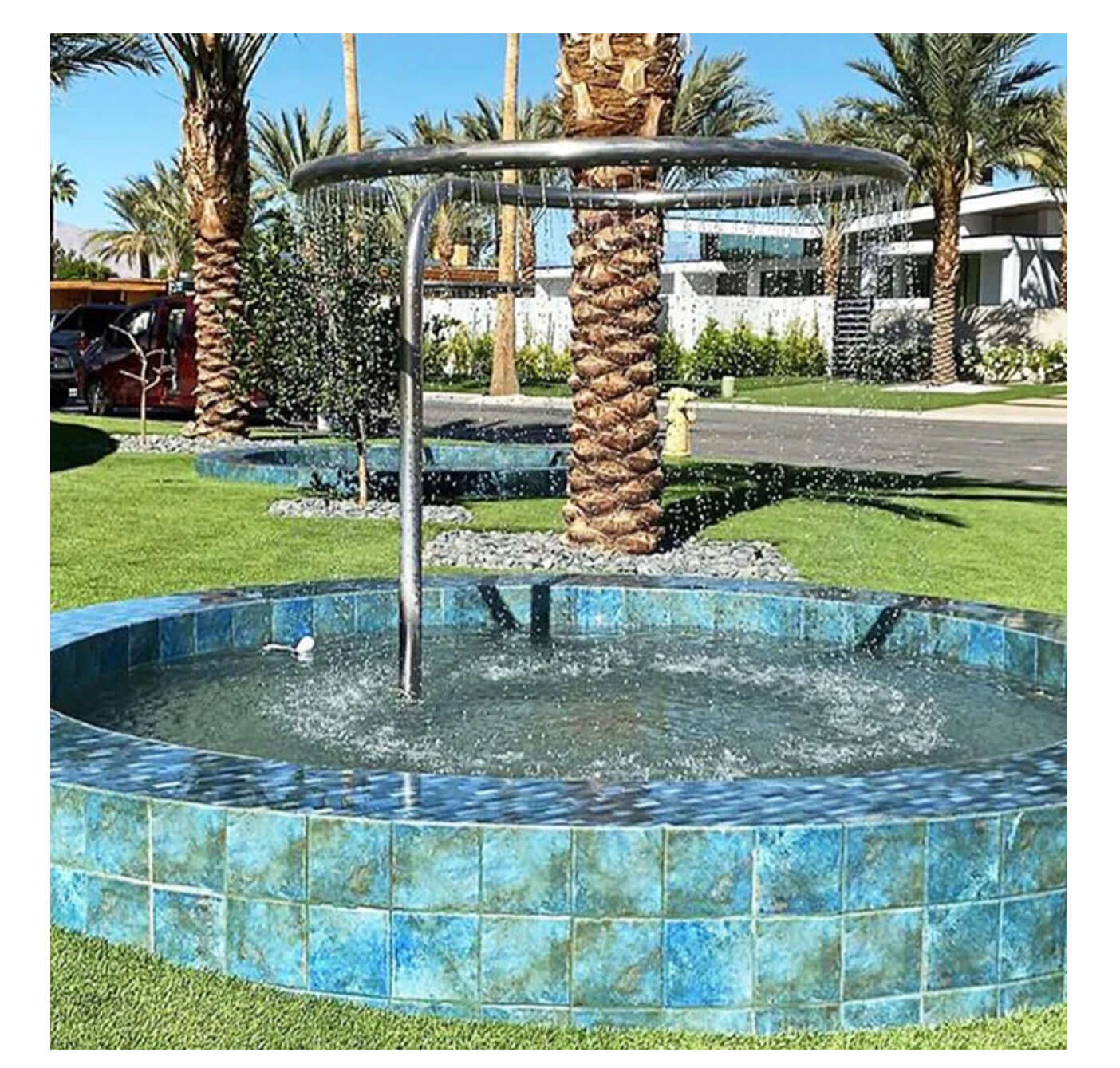 Circular blue tile fountain surrounded by palm trees and grass, creating a serene outdoor pool area.