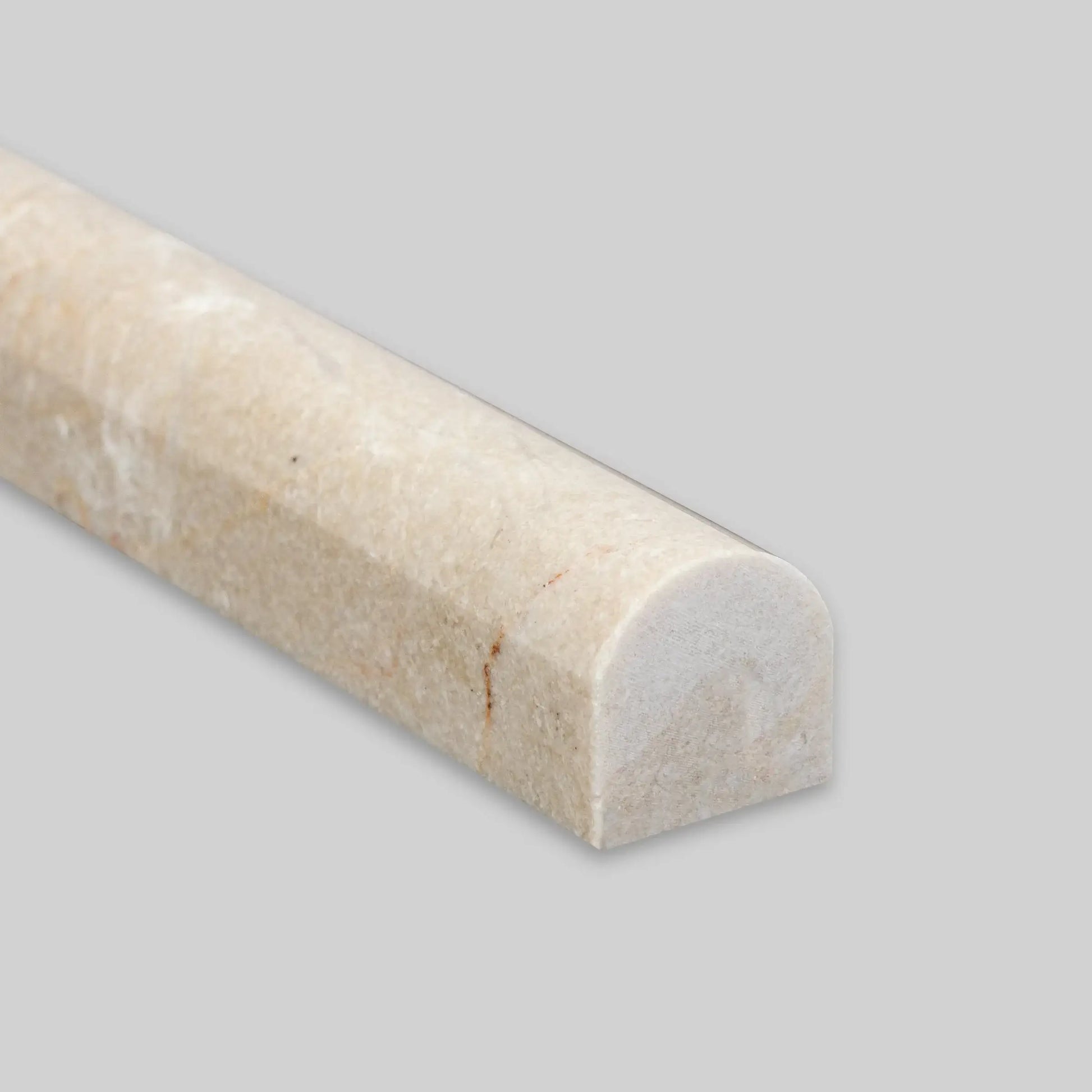 Close-up of a 1/2 x 12 polished Spanish Crema Marfil marble pencil liner on a gray background.