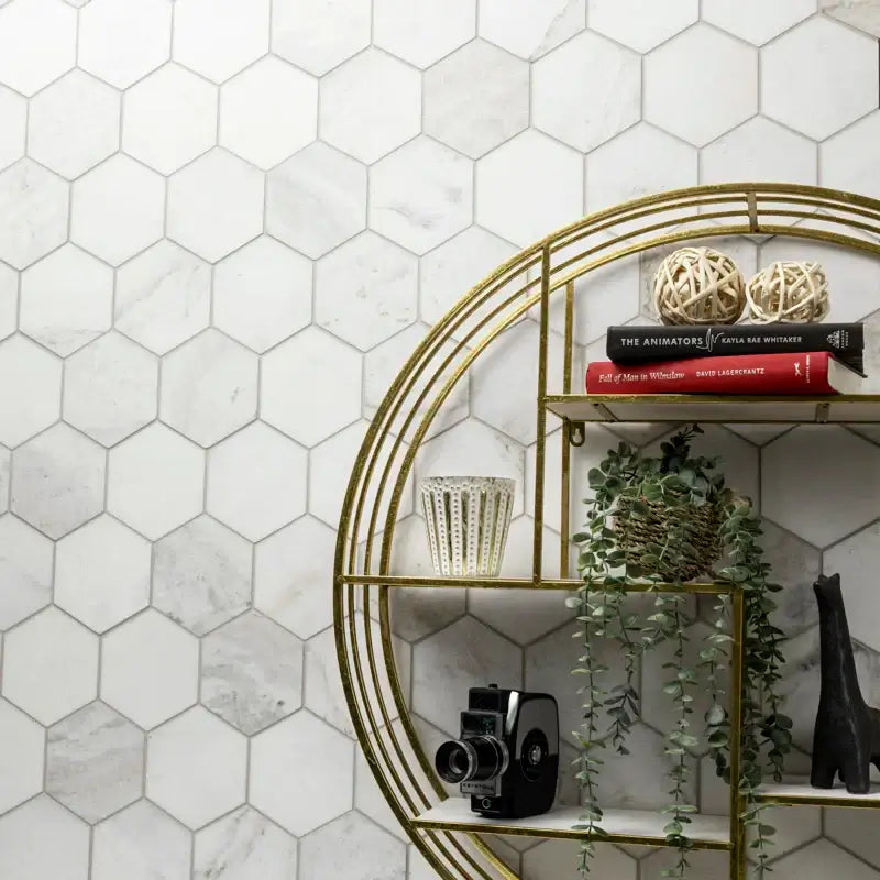 Honed Arabescato Venato white hexagon mosaic tile wall featuring stylish gold metal shelving.
