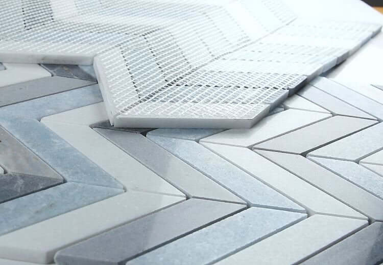 Chevron Deep Ocean Marble Mosaic tiles in blue, white, and grey, showcasing a sophisticated pattern on a flat surface.
