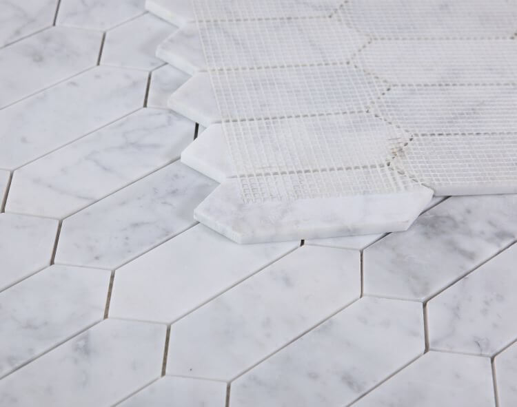Close-up of Elongated Hex Carrara Honed marble tiles, showcasing white hexagon pieces and a detailed pattern.