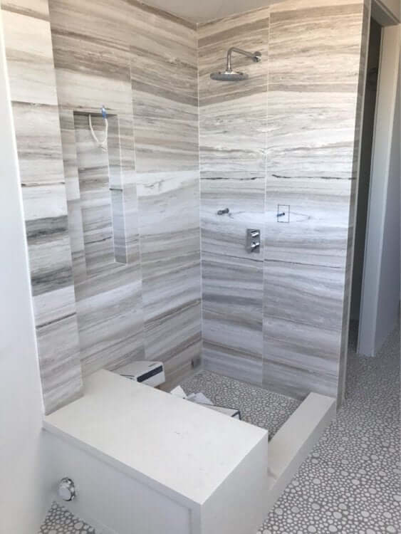 Modern shower design featuring sleek stone walls and pebble mosaic tile flooring.