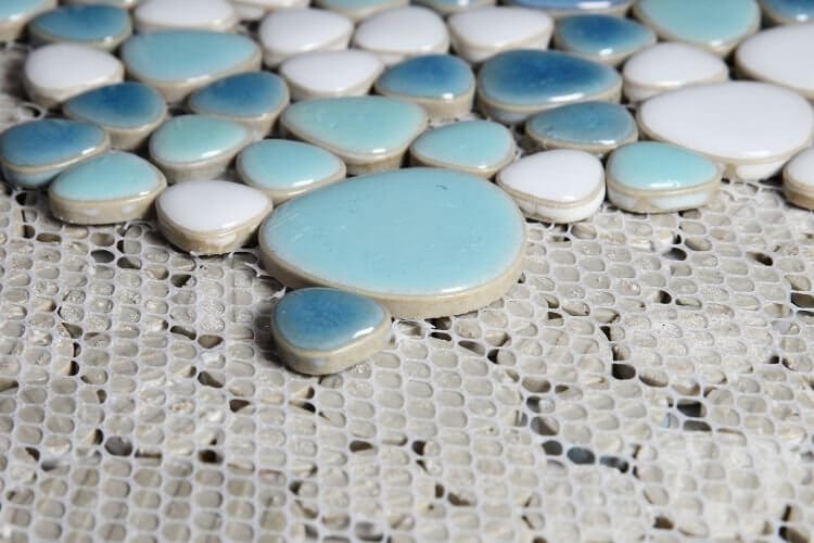 Close-up of blue and white pebble mosaic tiles on a textured surface, perfect for stylish decor and pools.