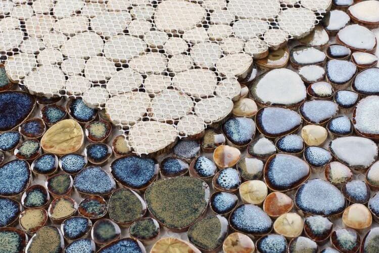 Close-up of Poseidon Olive 11.50 x 11.50 pebble mosaic tile showcasing smooth blue and earthy-toned porcelain pebbles.